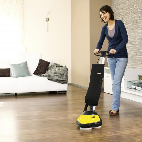 A woman uses a Kärcher FP303 Floor Polisher in a well-furnished living room with wooden flooring and large windows.