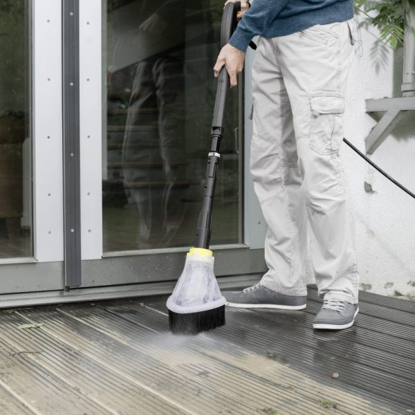 A person using a Splash Guard to clean a wooden deck outside a modern home.